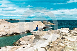 Woman sitting on the white cliffs of Sarakiniko. Milos Island, Greece.