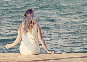 Woman sitting on wooden dock looking out at ocean