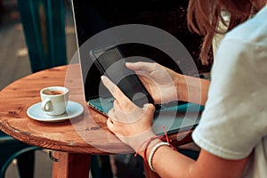 Woman sitting at wooden table in cafe using laptop and mobile phone