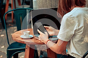 Woman sitting at wooden table in cafe using laptop and mobile phone