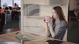 Woman sitting at the working place works with laptop than close it and relax with drink