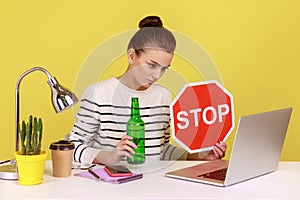 Woman sitting on workplace and having video conference, showing alcohol bottle and red stop sign.