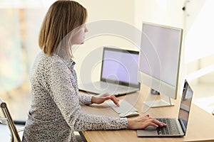 Woman sitting at workplace and working on laptop and pc in office