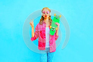 Woman with skateboard listens to music in wireless headphones in a pink denim jacket