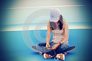 Woman skateboarder sit on skatepark stairs listening music