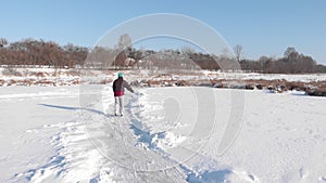 Woman is skating on frozen pond covered with snow. Young female rides in white figure skates on frozen lake in winter. Winter outd