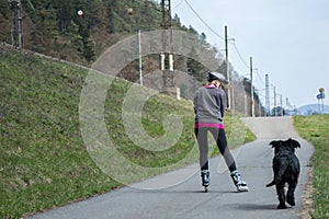 Woman is skating on rollerblades beside her dog outdoors.