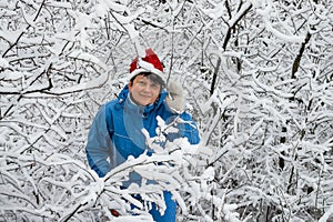 Woman in ski suit and cap of Santa Klaus in snow-covered wood