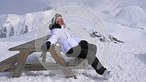 Woman Skier Pleasure to Relax in the Mountains on a Sunny Day Sitting on Bench