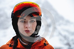 Woman skier on the slope of a mountain resort. Portrait of a young woman smiling in ski equipment, goggles and a helmet