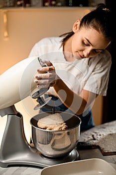 Woman skilfully prepares dough using modern electric kitchen stand mixer.