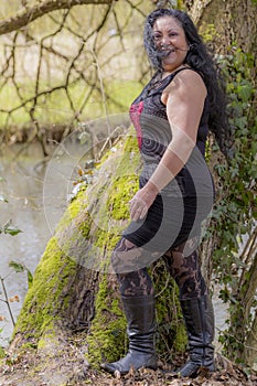 Woman with skirt and black blouse with her hair disheveled by the wind next to a trunk of a tree with moss