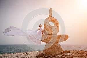 Woman sky stone. Lady stands on stone sculpture with ocean view. She is dressed in a white long dress, against the