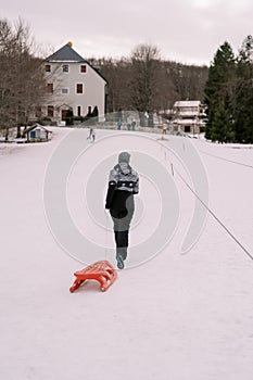 Woman with a sled on a rope walks along the top of a hill. Back view