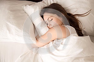 Woman sleeping in bed hugging soft white pillow