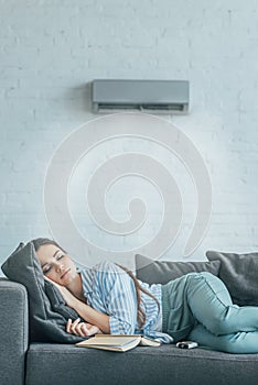 woman sleeping on couch with book and air conditioner blowing