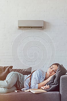 woman sleeping on sofa with book and air conditioner