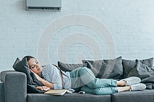 woman sleeping on sofa with book and air conditioner