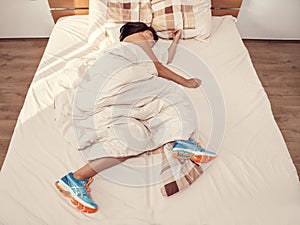 Woman sleeps in bed with her running shoes on photo