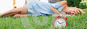 Woman sleeps on grass next to alarm clock