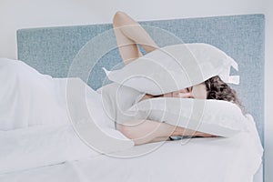 Woman sleeps pressing pillows to her ears and head.