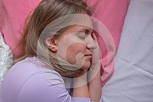 Woman sleeps on the side holding hands under the cheek. Close-up portrait of 40 years woman with calm and relax face sleeping on