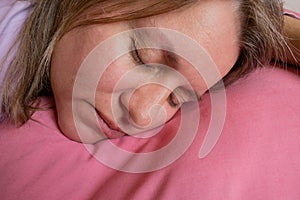 Woman sleeps on the stomach and embracing pillow. Close-up portrait of 40 years woman with calm and relax face sleeping on fresh