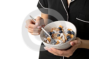 Woman in sleepwear holding bowl with whole wheat flakes, blueberry and coconut