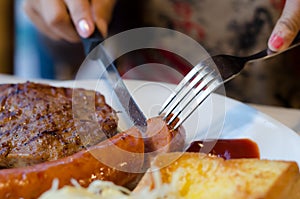 Woman slice sausage steak set on white dish photo
