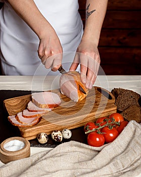 Woman slices bacon into thick pieces on a wooden board. Cooking breakfast, smoked whole bacon on a wooden board. Quail eggs, toma