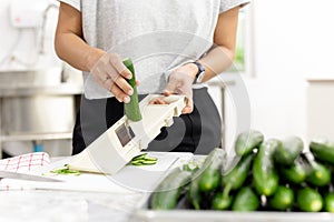 Woman slicing cucumber with vegetable slicer for salad.