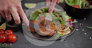 Woman slicing Fried grilled piece of Organic Tuna Steak on a black ceramic plate with salad