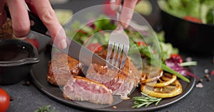 Woman slicing Fried grilled piece of Organic Tuna Steak on a black ceramic plate with salad