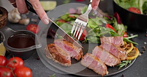 Woman slicing Fried grilled piece of Organic Tuna Steak on a black ceramic plate with salad