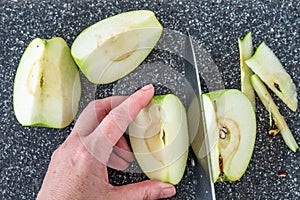 Woman slicing a green Granny Smith apple on a plastic man made faux gray granite cutting board, hands and chefs knife, apple quart