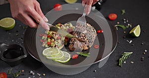 Woman slicing grilled fried tuna steak covered with sesame seeds on a plate with and traditional salsa garnish