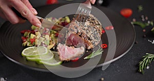 Woman slicing grilled fried tuna steak covered with sesame seeds on a plate with and traditional salsa garnish