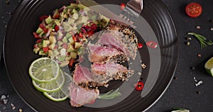 Woman slicing grilled fried tuna steak covered with sesame seeds on a plate with and traditional salsa garnish