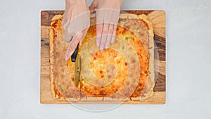 Woman slicing pizza using a pizza cutter. Vegetarian pizza with Mozzarella cheese topping close up on wooden board