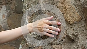 Woman sliding hand against old stone wall in slow motion. Female hand touching rough surface of rock