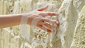 Woman sliding hand against old stone wall in slow motion. Female hand touching rough surface of rock