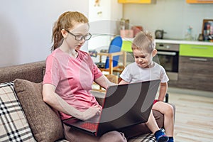 Woman with a small child on knees is sitting at a laptop. Remote work and receiving online education of home