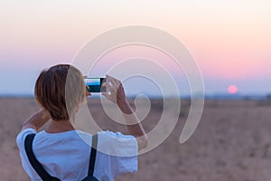 Woman smart phone photo at desert sunset. Tourist photographing the Namib desert, sunset romantic sky, travel destination in Namib