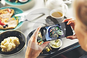 Woman with smart phone taking picture of food at restaurant