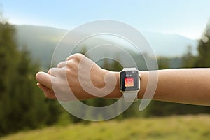 Woman with smart watch checking heart rate in health monitor app outdoors