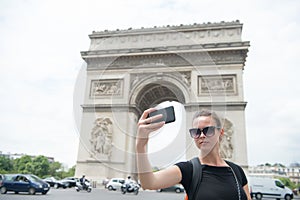 Woman with smartphone at arch monument in paris, france. Woman make selfie with phone at arc de triomphe. Vacation and sightseeing