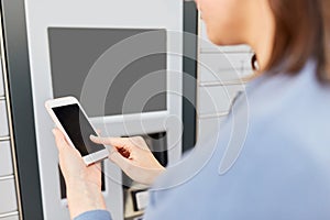 Woman with smartphone at automated parcel machine