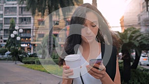 Woman with smartphone and coffee walking in the city, steadicam shot