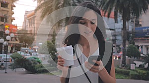 Woman with smartphone and coffee walking in the city, steadicam shot