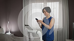 Woman with smartphone in hands is chatting online, watching news in internet while training on treadmill. Female is exercising on